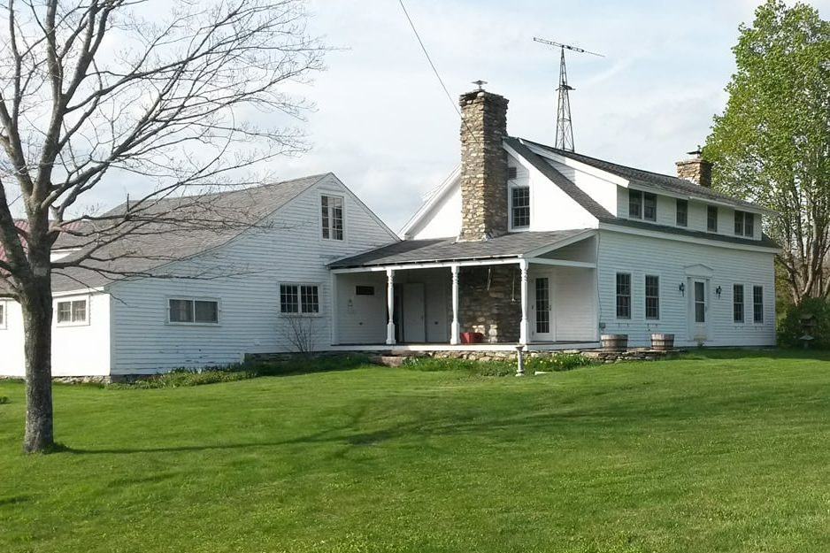 a white farmhouse with wood shed, seen from across a green lawn